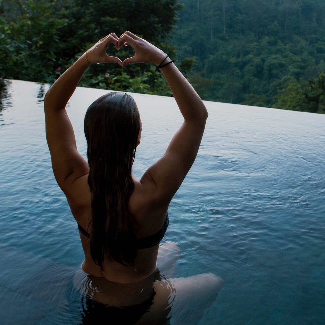 A woman sitting in the middle of a pool with her arms raised.