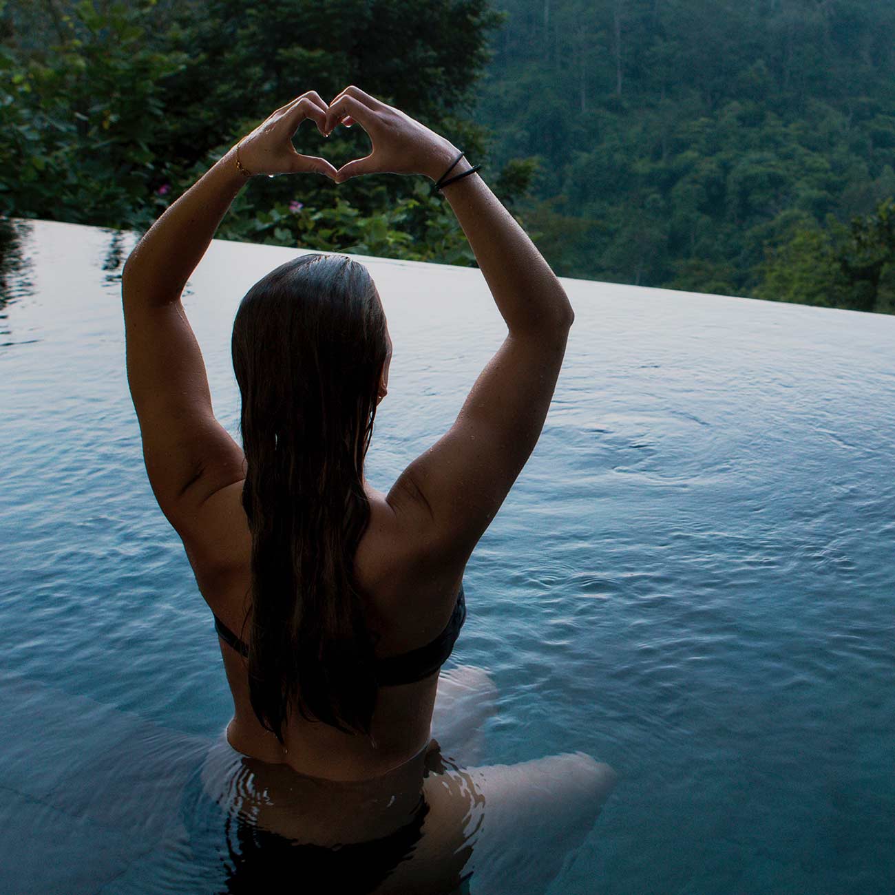 A woman sitting in the middle of a pool with her arms raised.