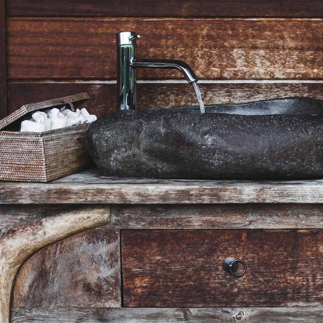 A sink with a wooden counter and a black stone