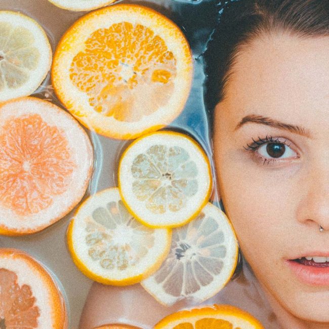 A woman with oranges and lemons in front of her face.