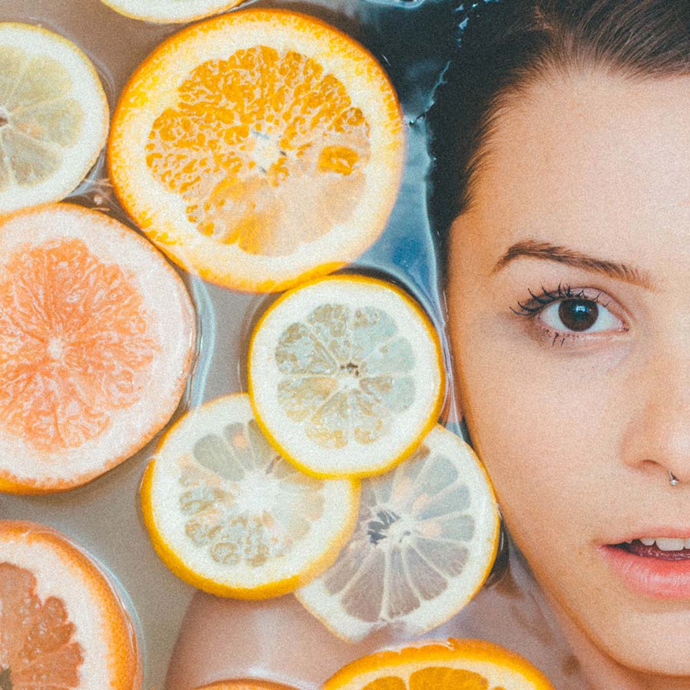 A woman with oranges and lemons in front of her face.
