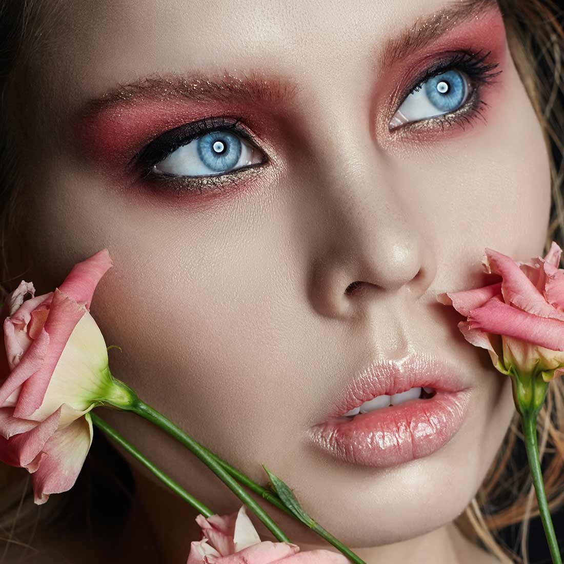 A woman with blue eyes and pink makeup holding flowers.