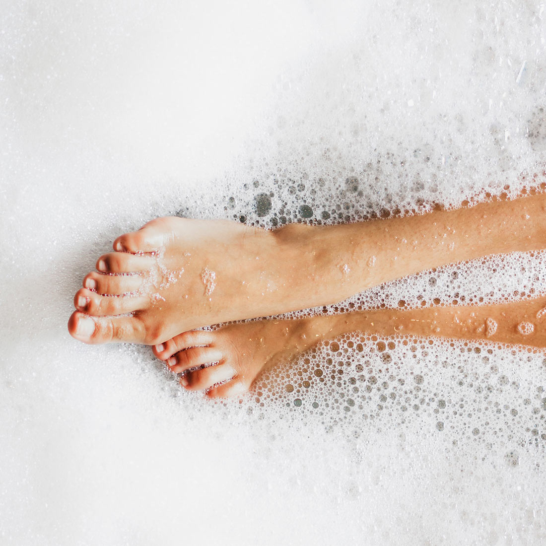 A person 's feet in the bath tub with foam.