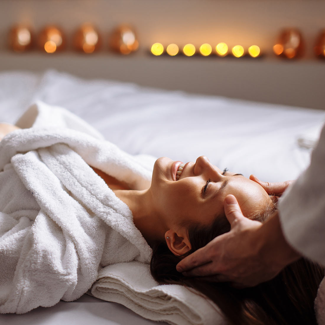 A woman laying on her stomach in bed with candles.